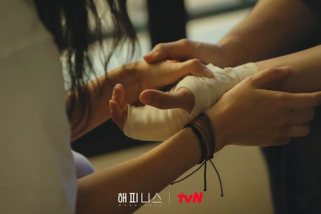 A screenshot from the Korean drama 'Happiness' showing a pair of hands holding each other. 